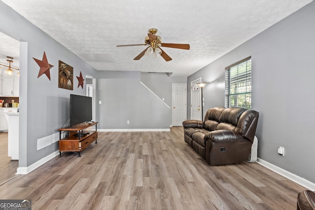 living area featuring light wood-type flooring, a textured ceiling, and ceiling fan