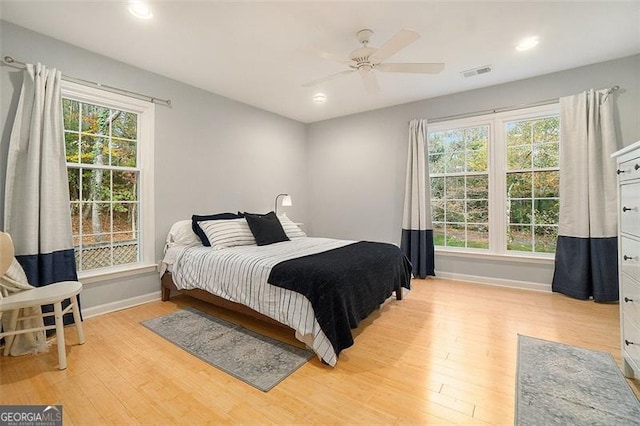 bedroom featuring ceiling fan, light hardwood / wood-style floors, and multiple windows