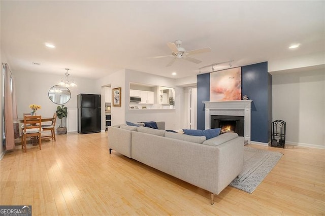 living room with ceiling fan with notable chandelier, track lighting, and light hardwood / wood-style floors