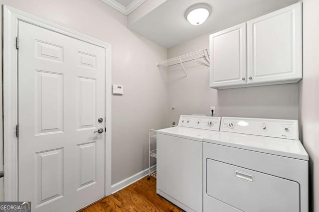 clothes washing area featuring dark hardwood / wood-style flooring, washer and dryer, ornamental molding, and cabinets