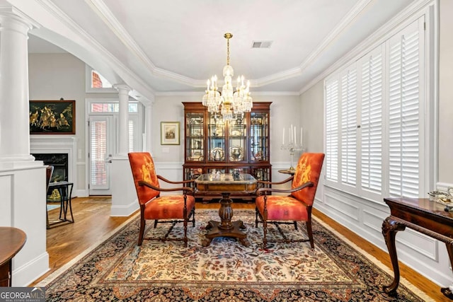 dining room featuring a chandelier, crown molding, wood-type flooring, and decorative columns