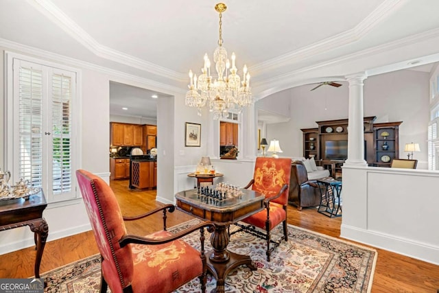 dining area featuring light hardwood / wood-style flooring, ceiling fan with notable chandelier, crown molding, and decorative columns