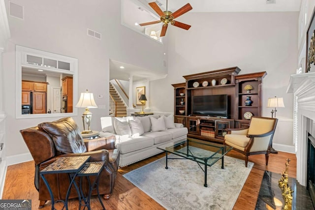 living room featuring a premium fireplace, a towering ceiling, hardwood / wood-style floors, and ceiling fan