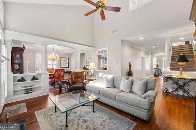 living room with ornate columns, dark hardwood / wood-style floors, a towering ceiling, built in features, and ceiling fan with notable chandelier