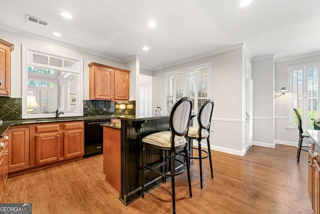 kitchen featuring decorative backsplash, sink, black dishwasher, light hardwood / wood-style flooring, and a breakfast bar area