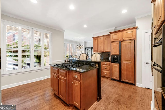 kitchen with a kitchen island, decorative light fixtures, dark stone countertops, light hardwood / wood-style floors, and gas cooktop