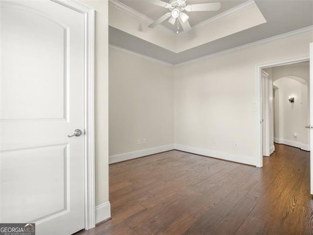 unfurnished room with a tray ceiling, dark wood-type flooring, ornamental molding, and ceiling fan