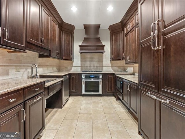 kitchen featuring custom exhaust hood, tasteful backsplash, light tile patterned floors, appliances with stainless steel finishes, and light stone countertops