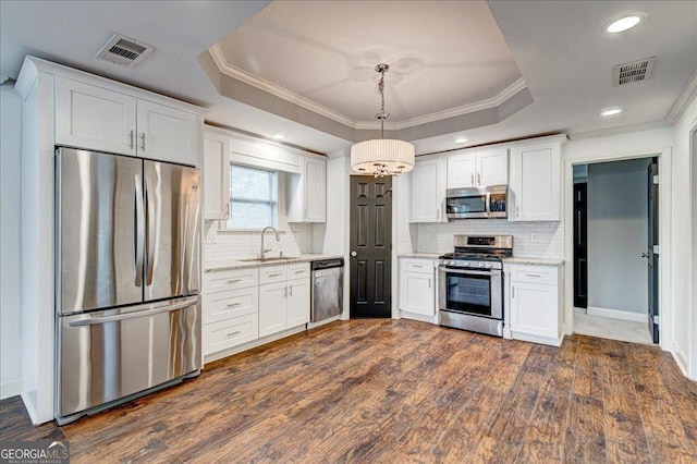 kitchen with a tray ceiling, pendant lighting, white cabinets, and stainless steel appliances