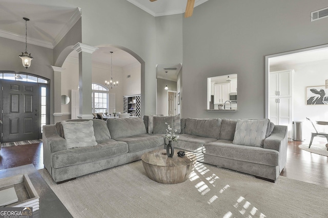 living room with ceiling fan with notable chandelier, sink, a towering ceiling, ornamental molding, and decorative columns