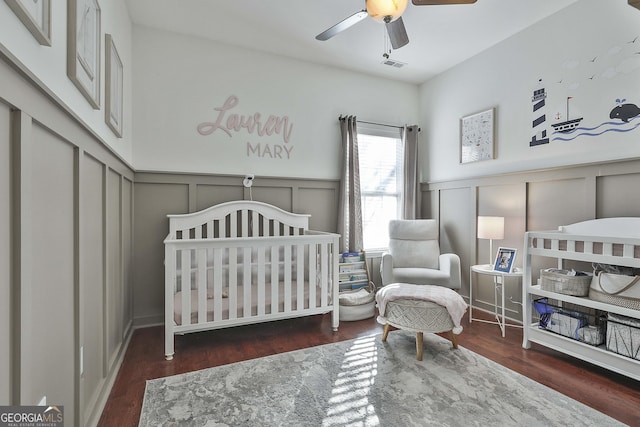 bedroom featuring ceiling fan, dark wood-type flooring, and a crib