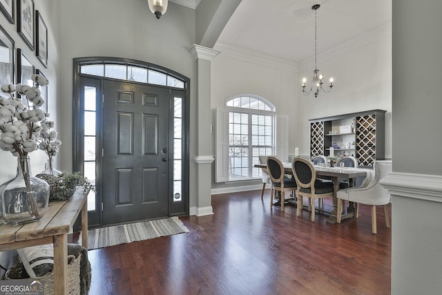 entrance foyer with dark wood-type flooring, ornamental molding, and a notable chandelier