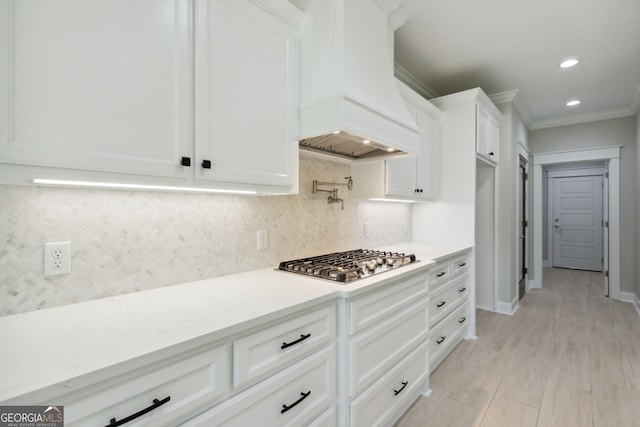 kitchen with white cabinetry, backsplash, ornamental molding, custom range hood, and stainless steel gas stovetop