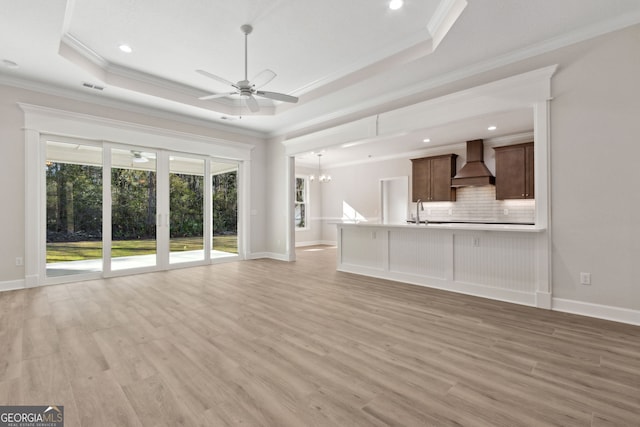 unfurnished living room with a tray ceiling, ceiling fan with notable chandelier, visible vents, and light wood-type flooring