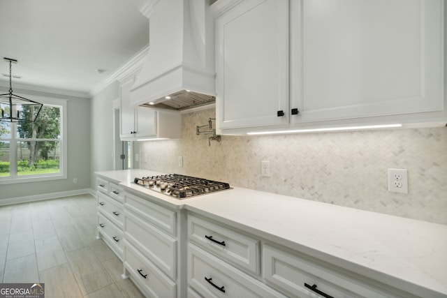 kitchen featuring hanging light fixtures, stainless steel gas cooktop, custom exhaust hood, and white cabinets