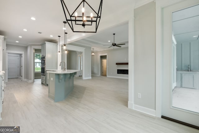 kitchen with pendant lighting, white cabinets, a kitchen breakfast bar, ornamental molding, and a center island with sink