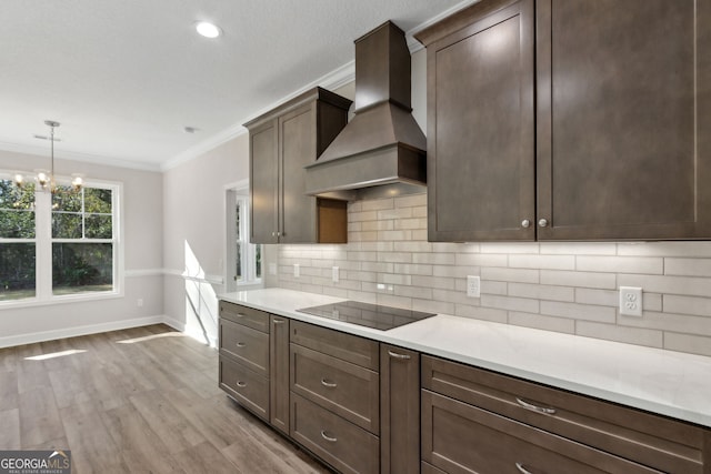 kitchen with light countertops, custom range hood, crown molding, black electric stovetop, and backsplash