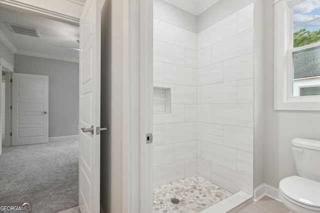 bathroom featuring ornamental molding, toilet, and a tile shower