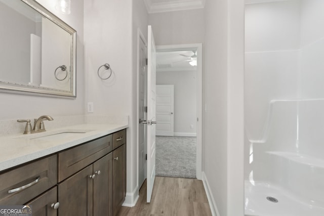 bathroom with baseboards, ornamental molding, wood finished floors, vanity, and a shower