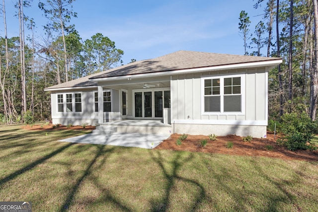 back of house featuring board and batten siding, ceiling fan, roof with shingles, a lawn, and a patio