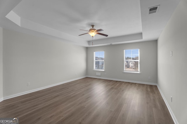 unfurnished room featuring a tray ceiling, ceiling fan, and dark hardwood / wood-style flooring