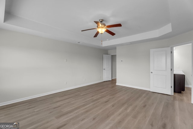 unfurnished room featuring a tray ceiling, ceiling fan, and light wood-type flooring