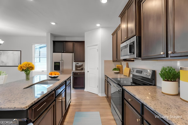 kitchen with dark brown cabinetry, light stone counters, light hardwood / wood-style flooring, decorative backsplash, and appliances with stainless steel finishes