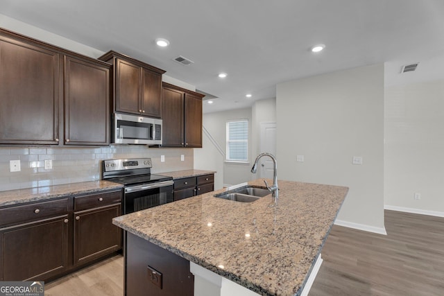 kitchen featuring sink, stainless steel appliances, light stone counters, an island with sink, and decorative backsplash