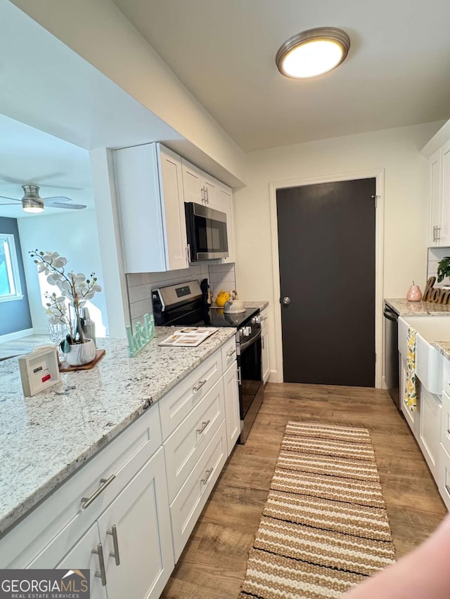 kitchen with white cabinets, appliances with stainless steel finishes, tasteful backsplash, and wood-type flooring