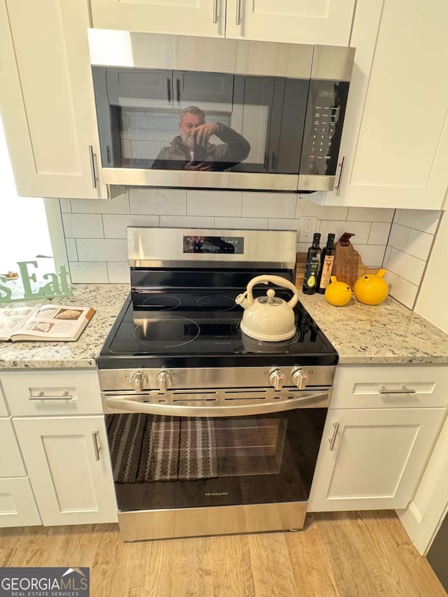 kitchen featuring light stone countertops, stainless steel appliances, white cabinetry, and tasteful backsplash