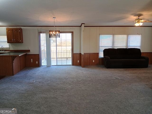 unfurnished living room featuring ceiling fan with notable chandelier, carpet floors, crown molding, and sink