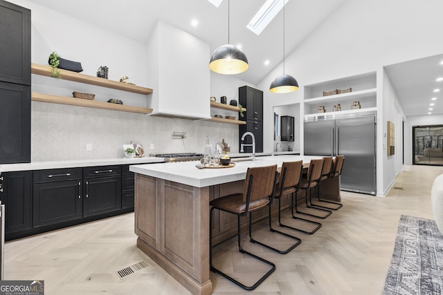 kitchen with a kitchen island with sink, high vaulted ceiling, stainless steel built in fridge, a skylight, and light parquet flooring