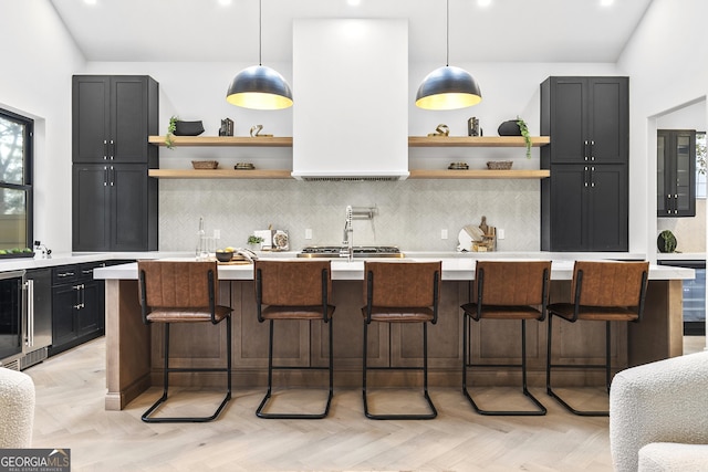 kitchen with a breakfast bar area, light parquet floors, an island with sink, and pendant lighting