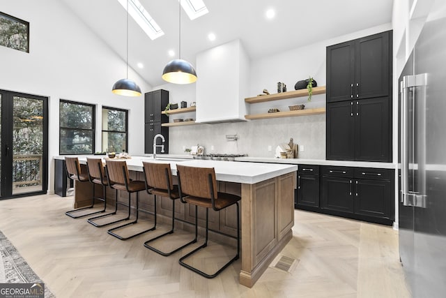 kitchen featuring a skylight, high end fridge, light parquet flooring, hanging light fixtures, and an island with sink