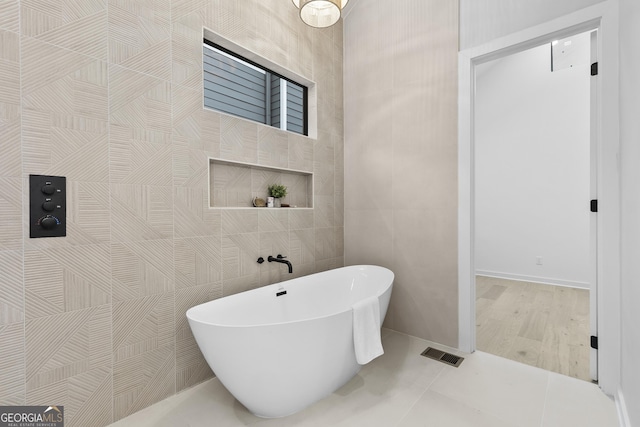 bathroom with a washtub, tile patterned flooring, and tile walls