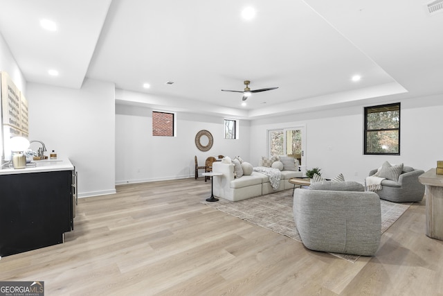 living room with a tray ceiling, ceiling fan, light hardwood / wood-style floors, and sink