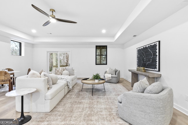 living room with a raised ceiling, ceiling fan, and light hardwood / wood-style flooring