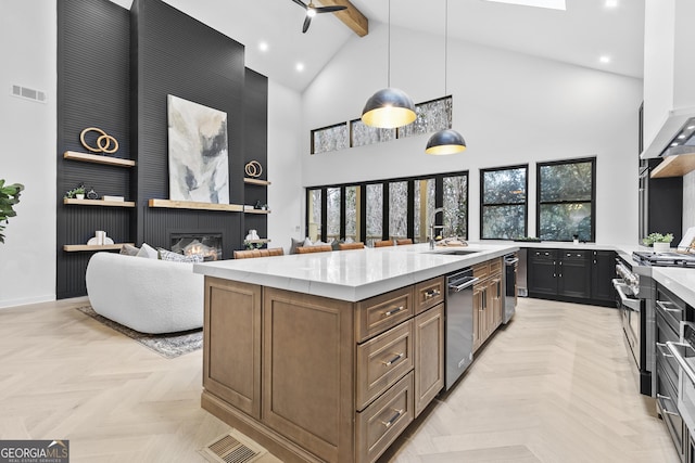 kitchen with stainless steel appliances, light parquet floors, sink, a center island with sink, and hanging light fixtures