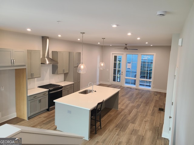 kitchen featuring gas stove, ceiling fan, sink, wall chimney range hood, and pendant lighting