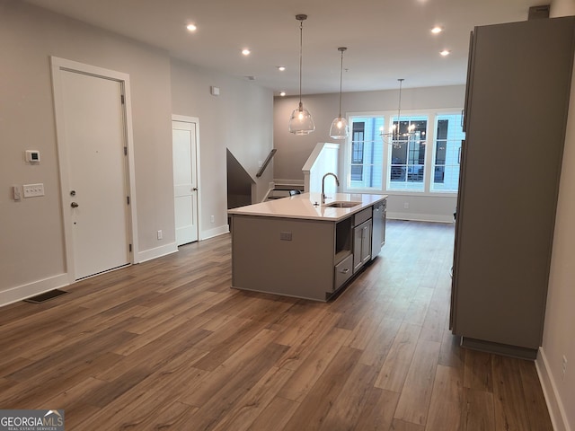 kitchen with sink, dark wood-type flooring, hanging light fixtures, gray cabinets, and a kitchen island with sink