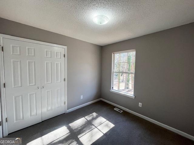 unfurnished bedroom with dark colored carpet, a textured ceiling, and a closet