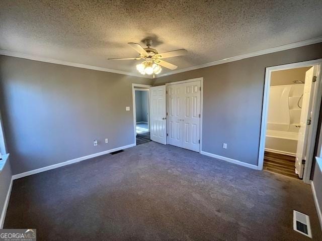 unfurnished bedroom featuring dark colored carpet, crown molding, ensuite bath, ceiling fan, and a textured ceiling