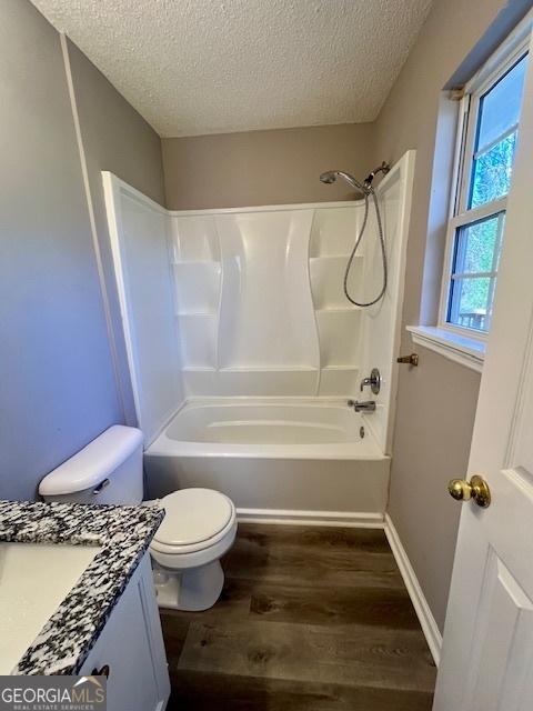 full bathroom featuring vanity, a textured ceiling,  shower combination, hardwood / wood-style floors, and toilet