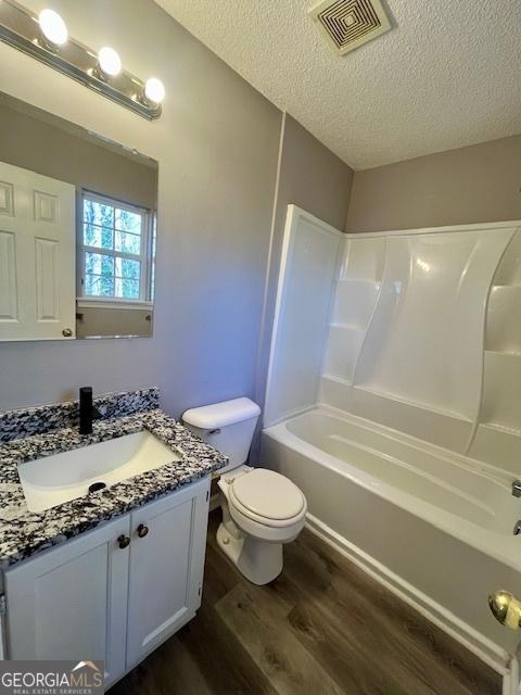 full bathroom with shower / bathing tub combination, a textured ceiling, toilet, vanity, and hardwood / wood-style flooring