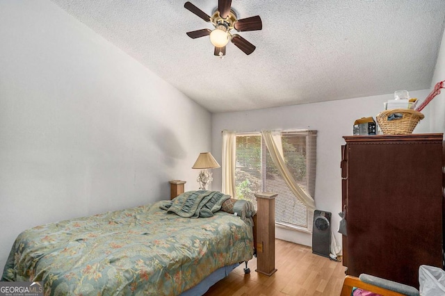 bedroom with ceiling fan, lofted ceiling, a textured ceiling, and light wood-type flooring