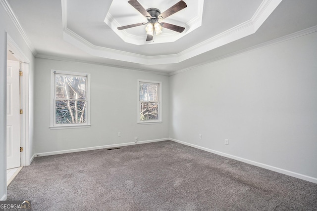 carpeted empty room with ceiling fan, a wealth of natural light, a tray ceiling, and ornamental molding