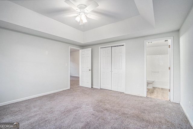 unfurnished bedroom featuring ensuite bathroom, carpet, ceiling fan, and a tray ceiling