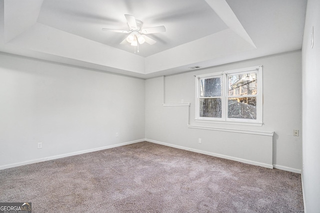 carpeted empty room featuring ceiling fan and a raised ceiling