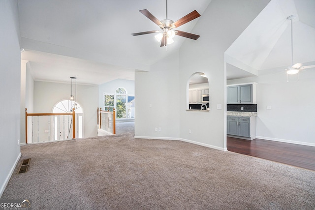 unfurnished living room featuring ceiling fan, high vaulted ceiling, and dark colored carpet