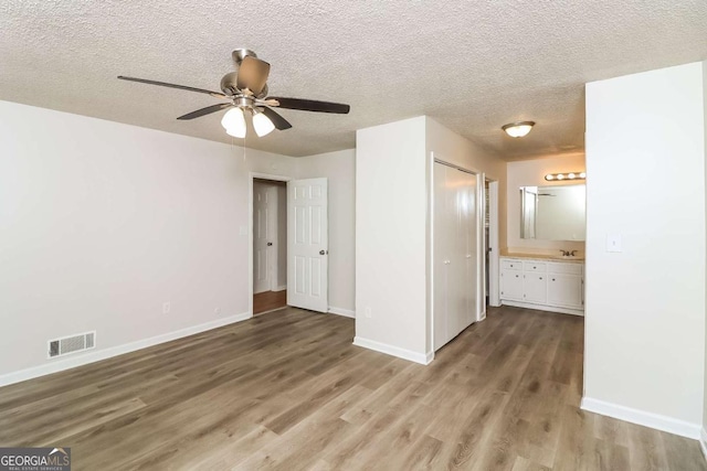 unfurnished bedroom with ensuite bathroom, a textured ceiling, ceiling fan, sink, and hardwood / wood-style flooring